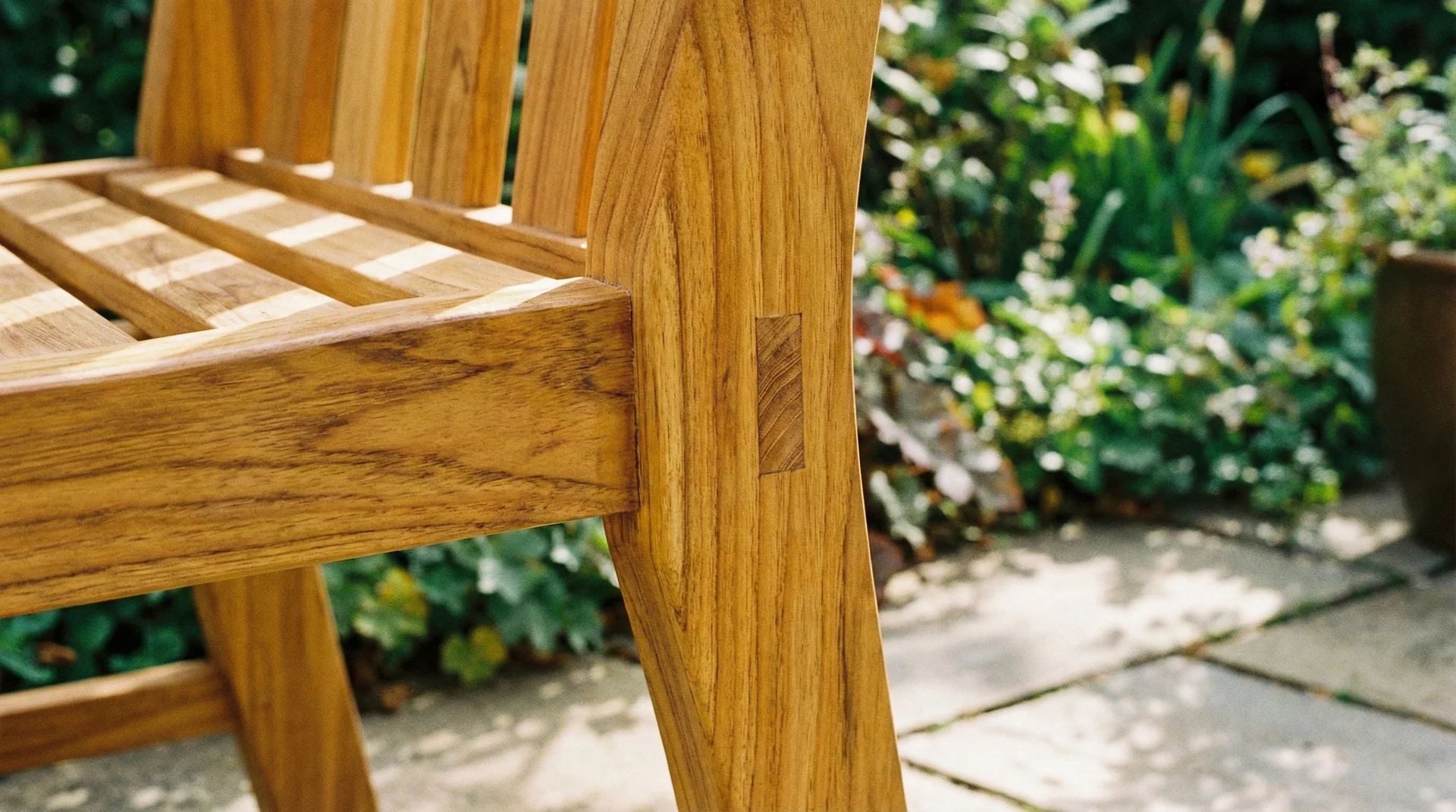 Close-up of a durable teak wood outdoor chair featuring a traditional mortise and tenon joint and rich wood grain.