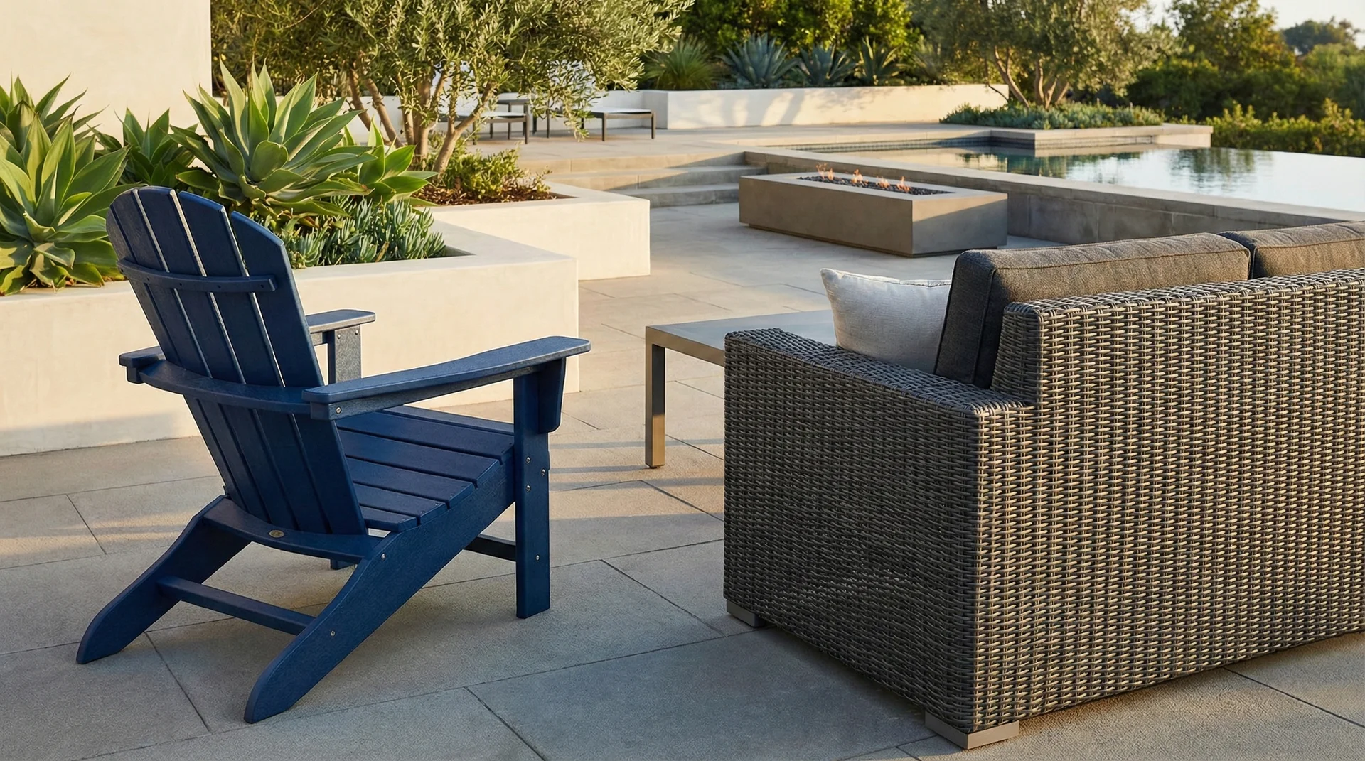 A close-up of a blue HDPE Adirondack chair and a grey resin wicker sofa on a sunny patio.