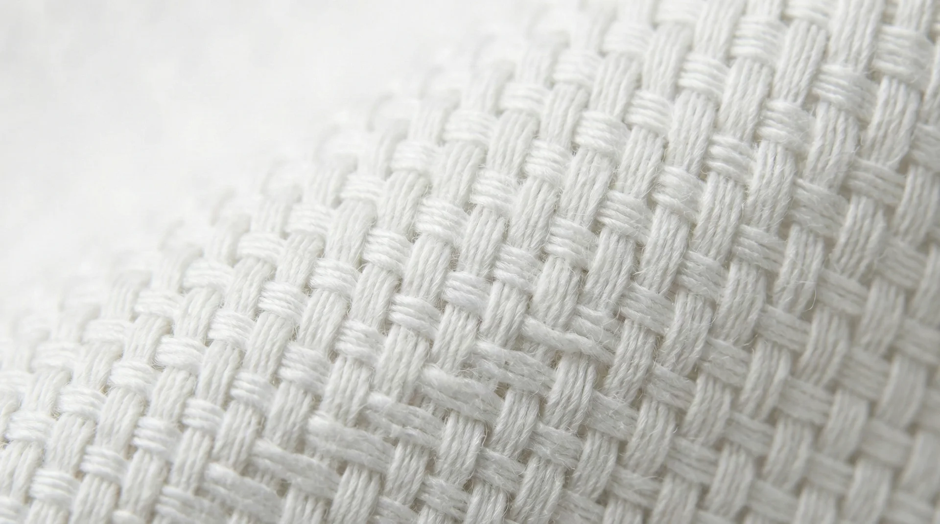 A detailed macro shot of a white cotton fabric showing the precise grid of horizontal and vertical threads.