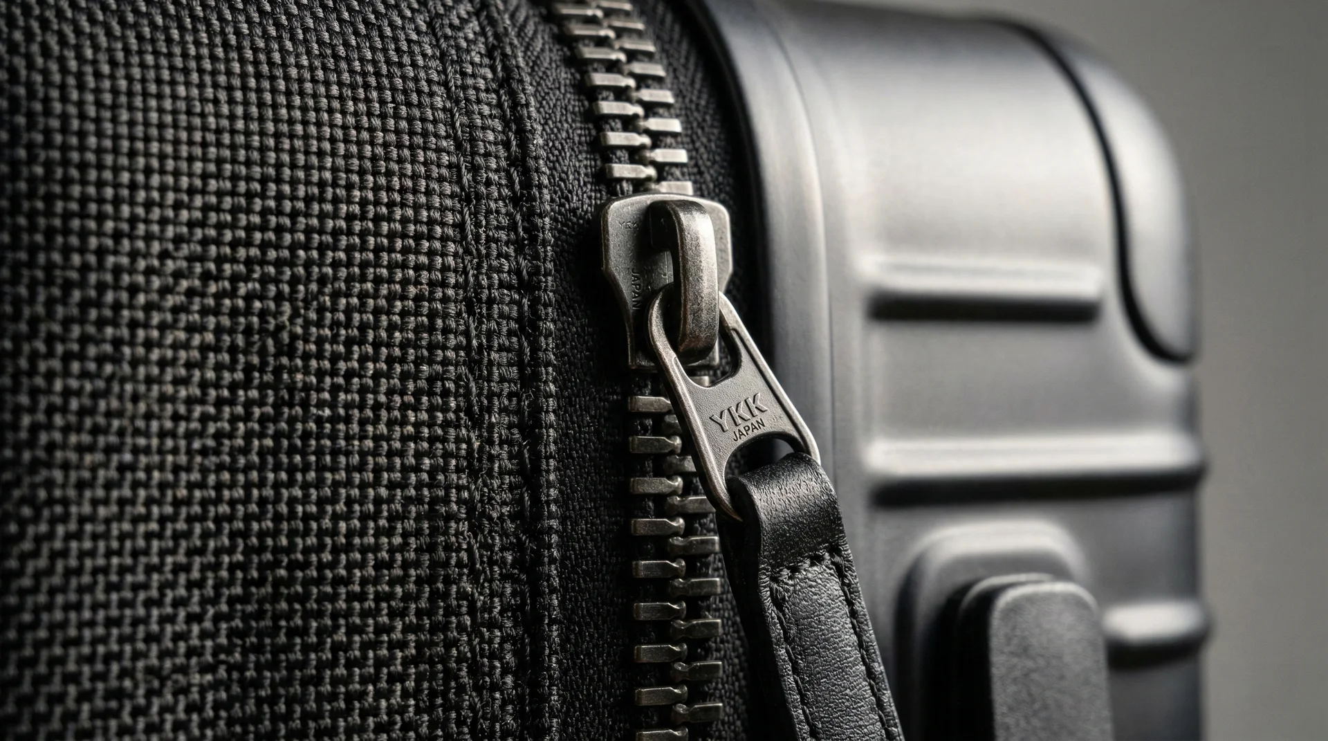 A detailed close-up of ballistic nylon fabric, a polycarbonate shell, and a heavy-duty YKK zipper on a suitcase.